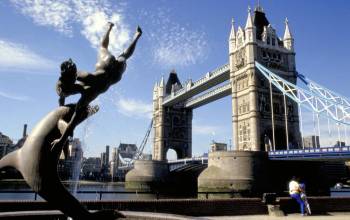 Statue of a dolphin playing with a boy next to Tower Bridge and the River Thames